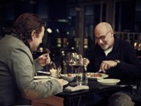 Zdjęcie przedstawiające aktorów Pawła Królikowskiego i Piotra Machalicę siedzących przy stole